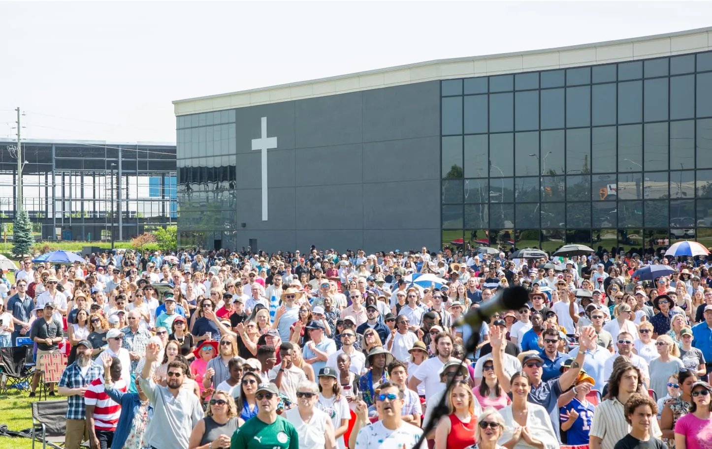 An outdoor church service taking place next to the building; people raising hands in worship